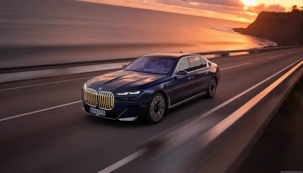 2026 BMW i7 electric sedan driving on coastal highway at golden hour sunset