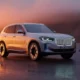 2027 BMW iX3 electric SUV parked on a dramatic mountain road at sunset