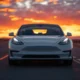 2026 Tesla Model 3 electric sedan front three-quarter view on open highway at sunset