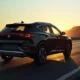 2026 MG IM6 electric SUV in black on a coastal road at golden hour rear three-quarter view