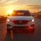2026 MG S5 EV in white driving on a coastal highway at golden hour, front three-quarter cinematic view.